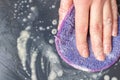 A female hand washes the dishes, a black frying pan with a lilac sponge with foam, close-up, top view Royalty Free Stock Photo