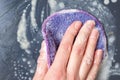 A female hand washes the dishes, a black frying pan with a lilac sponge with foam, close-up, top view Royalty Free Stock Photo