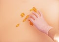 Female hand wear pink nitrile glove and taking yellow capsules from the table. Fistful of vitamin d3 above neutral background