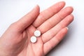 Female hand on white background holds two white pills. Dose of medicines