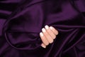 Female hand with white nail design. White nail polish manicure. Woman hand on dark purple satin fabric background Royalty Free Stock Photo