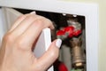 A female hand with white nails opens a white door in the recess of the bathroom wall, behind which pipes, counters and valves Royalty Free Stock Photo