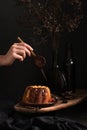 Female hand with wooden spoon drizzling chocolate icing on easter or christmas bund cake, dark mood photography