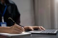 Female hand working search page on computer and writing on a notepad with a pen in the office. on the wooden desk there a graph Royalty Free Stock Photo