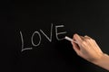 Female hand write word Love on blackboard with white chalk