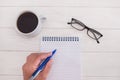Female hand are writing in a blank notebook on a white wooden background. Glasses and a cup of coffee. Flat lay Royalty Free Stock Photo