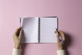 Female hand writing in blank open spiral notebook with pen on pastel pink background. Top view, copy space. Education Royalty Free Stock Photo