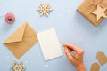 Female hand writing Christmas invitation card mockup over blue background with festive Christmas decorations, confetti, star, Royalty Free Stock Photo