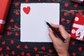 Female hand writing on an empty white paper decorated with valentine love heart