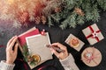 Female hand writing a letter to Santa on dark background with Christmas gift boxes, Fir branches, light.