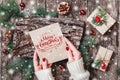 Female hand writing a letter to Santa on wooden background with Christmas gifts, bark texture, Fir branches, pine cones, red decor Royalty Free Stock Photo