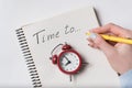 Female hand writing in notebook words TIME TO. Top view of notepad, retro alarm clock and hand