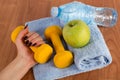 Female hand with yellow dumbbell and fresh green apple and water bottle on blue towel on wooden floor Royalty Free Stock Photo