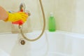 A female hand in a yellow rubber glove cleans the surface of the bathroom, faucet, shower.