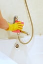 A female hand in a yellow rubber glove cleans the surface of the bathroom, faucet, shower.