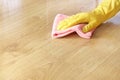 A female hand in a yellow rubber glove washes a wooden parquet floor with a pink microfiber cloth.