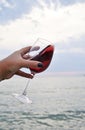 Female handd with wine glass with red wine on the beach at sunset.