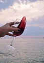 Female handd with wine glass with red wine on the beach at sunset.