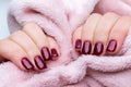 Female hands with beautiful manicure - dark red glittered nails with pink fluffy fabric, textile. Selective focus