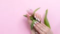 Female hands with beautiful manicure - white ivory oval nails with tulip flower on pink paper background with copy space Royalty Free Stock Photo