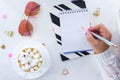 female hands with a beautiful manicure write with a pen in a notebook and a white cup with coffee with marshmallows