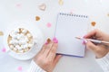 female hands with a beautiful manicure write with a pen in a notebook and a white cup with coffee with marshmallows Royalty Free Stock Photo