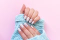 Female hands in blue knitted sweater with beautiful manicure - white ivory nails with flower on pink paper background