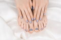 Female hands with blue nail design. Glitter blue nail polish pedicure. Female hands and feet on white fabric background Royalty Free Stock Photo