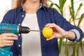 Female hands in a blue shirt hold a screwdriver with a drill and a bright lemon against the background of a light window and green Royalty Free Stock Photo