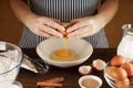 Female hands breaking egg into ceramic bowl on kitchen table with tableware.