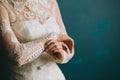 Female hands of the bride fasten buttons on the sleeve on a beautiful lace white wedding vintage dress close-up, morning preparati