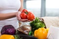 Female hands of a caucasian cook holding red tomato bunch over kitchen worktop with fresh grocery and rye bread on it.