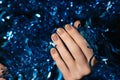 Female hands with Christmas nail design. Beige nail polish manicured hands. Female hand on holding blue New Year tinsel