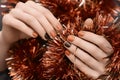 Female hands with Christmas nail design. Orange nail polish manicure. Female hand on brown New Year tinsel background