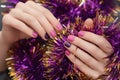 Female hands with Christmas nail design. Pink nail polish manicure. Female hand on purple New Year tinsel background