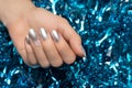 Female hands with Christmas nail design. Silver nail polish manicure. Female hand on blue New Year tinsel background