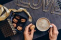 Female hands with coffee cup and macaron cake. Box with sweets and wire word Love on gray napkin background. Romantic breakfast