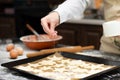 The female hands of the cook sprinkle sugar on puff pastry lying on parchment on a baking sheet at home in the kitchen. Nearby lie