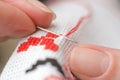 Close-up of female hands cross-stitching on white canvas. A woman embroiders the national symbols of Ukraine with a cross
