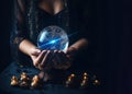 Female hands with crystal ball and burning candles in the dark, prediction session.