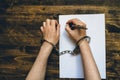 Female hands cuffed signing confession, top view Royalty Free Stock Photo