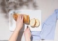 Female hands cut fresh white loaf bread on a white cutting board. Summer flat lay, shadows on table Royalty Free Stock Photo