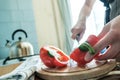 Female hands cut red pepper into two parts with a large knife, on a cutting wooden board, in the kitchen. Royalty Free Stock Photo