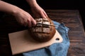 Female hands cut a round loaf of rye bread on a board on a dark wooden background, rustic style Royalty Free Stock Photo