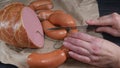 Female hands cut two pieces of sausage from a bunch of sausages on paper