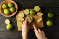 Female hands cuts lime on cutting board, top view