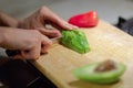 Female hands cutting fresh organic avocado with knife on wooden board in kitchen. Red bell pepper on background. Royalty Free Stock Photo