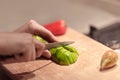 Female hands cutting fresh organic avocado with knife on wooden board in kitchen. Red bell pepper on background. Royalty Free Stock Photo