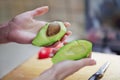 Female hands cutting fresh organic avocado to two peaces, pip inside. The knife and red bell pepper on wooden board in kitchen. Royalty Free Stock Photo