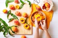 Female hands cutting fresh sweet peaches. Peaches whole fruits leaves, half peach, peach slices on white wooden kitchen table.